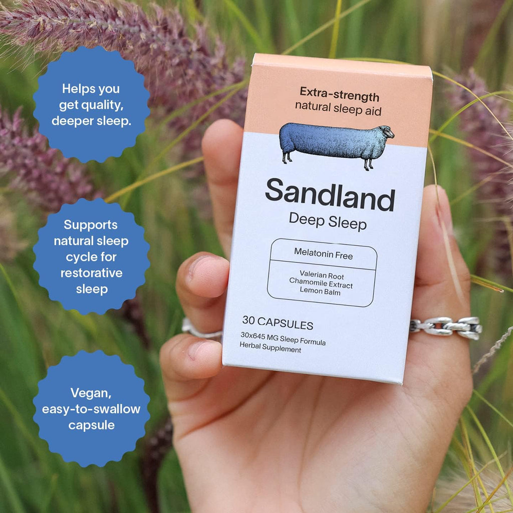 Hand holding a box of Sandland Deep Sleep supplement with natural background