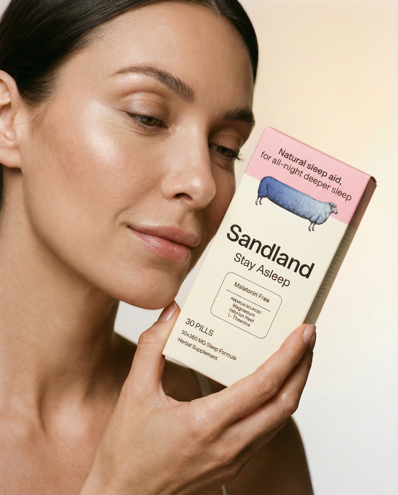 Woman holding a box of Sandland Stay Asleep supplement against a neutral background